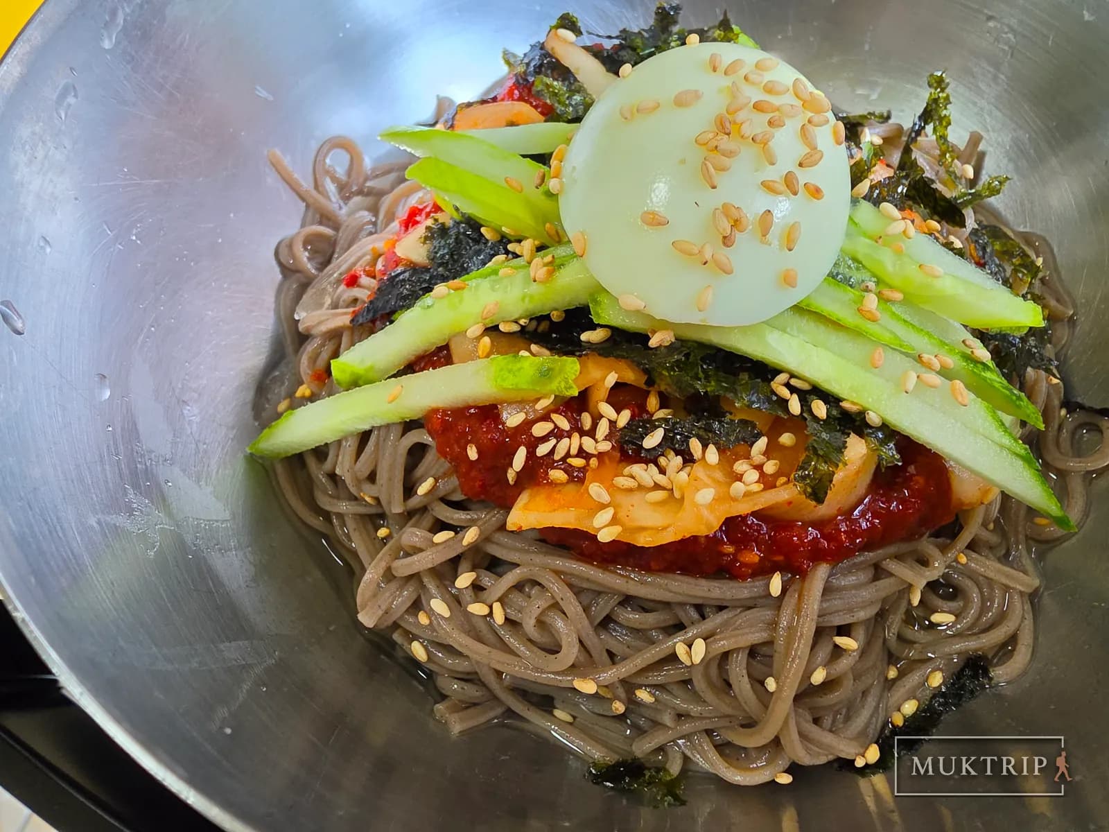 Bibim makguksu topped with cucumber, boiled egg, and crumbled seaweed
