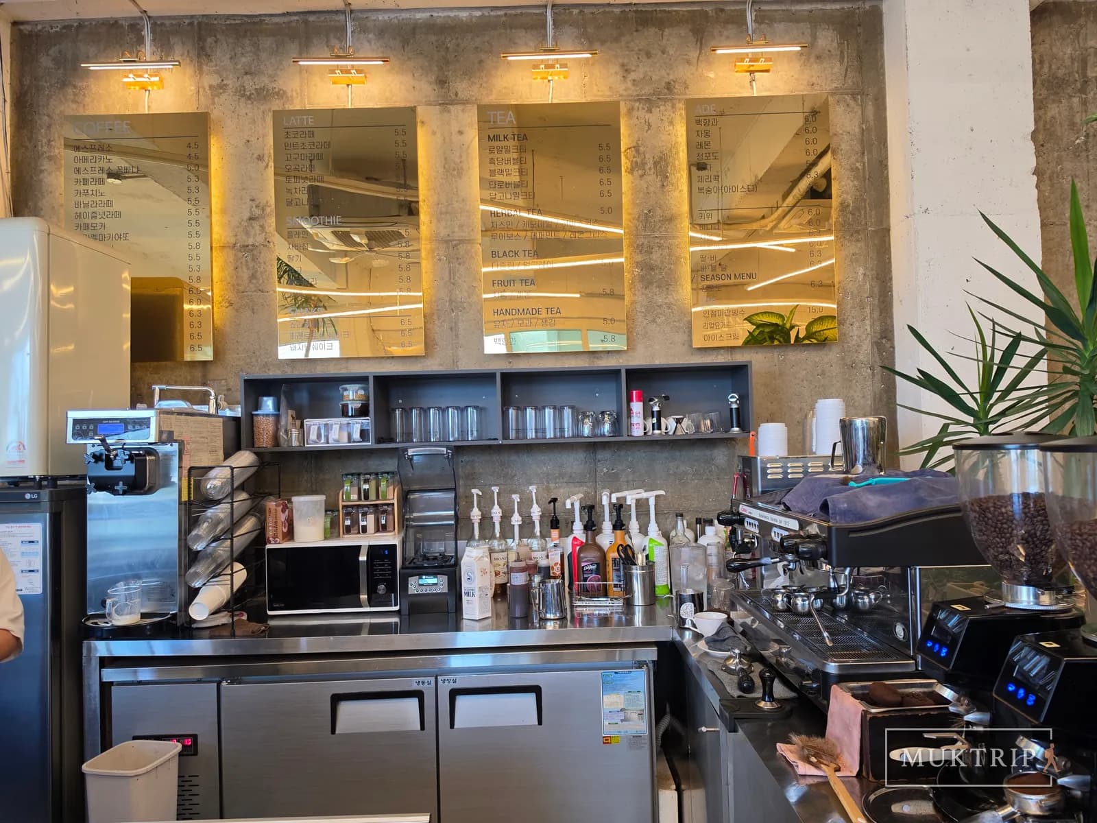 A coffee bar with an exposed concrete wall and golden menu boards