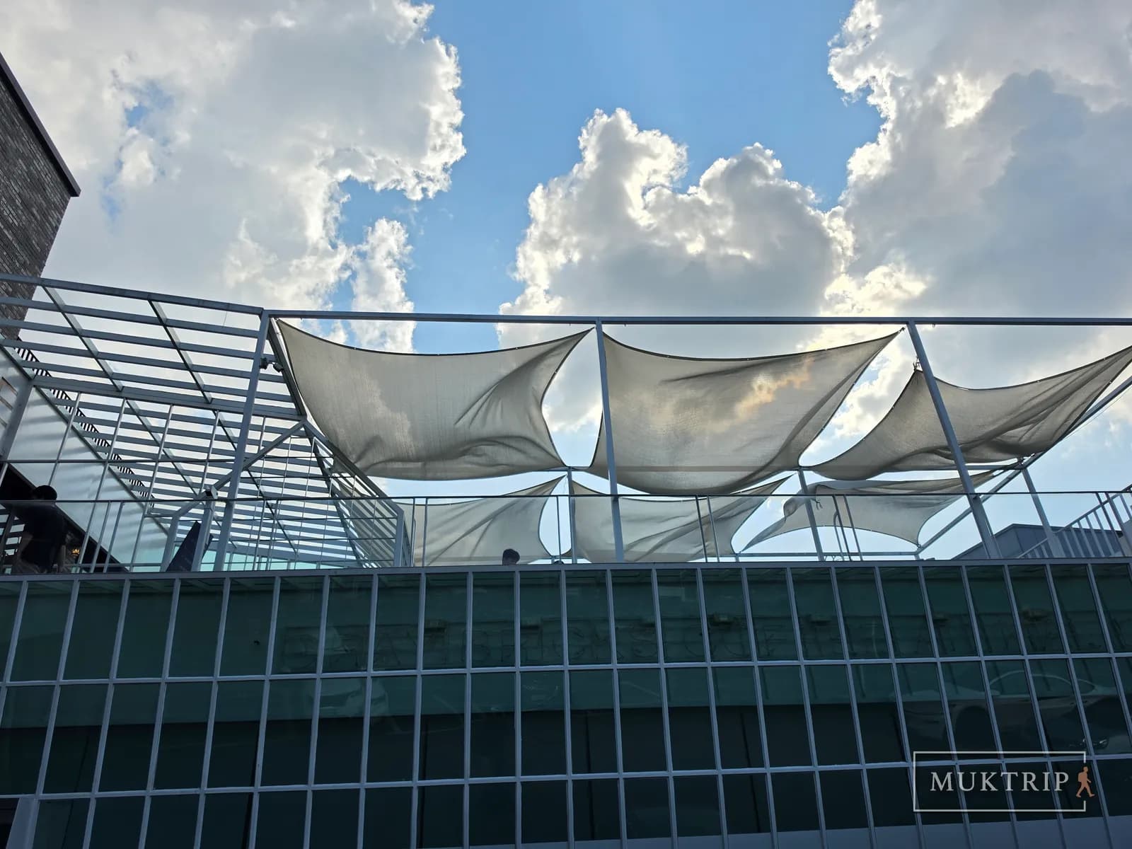 A rooftop seating area with shade sails stretched out under white clouds