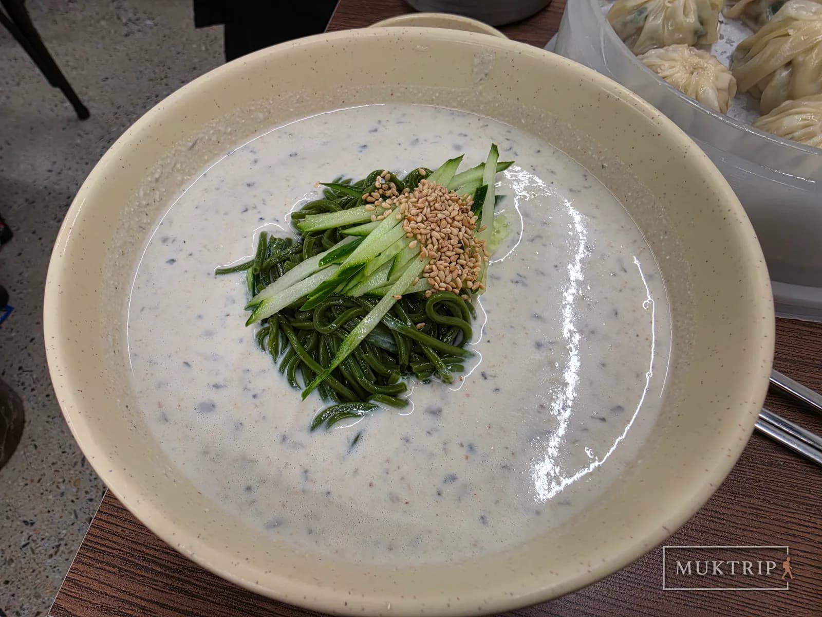 黄緑色の豆乳スープに浸かった緑の麺ときゅうりの細切り、ごまのトッピング
