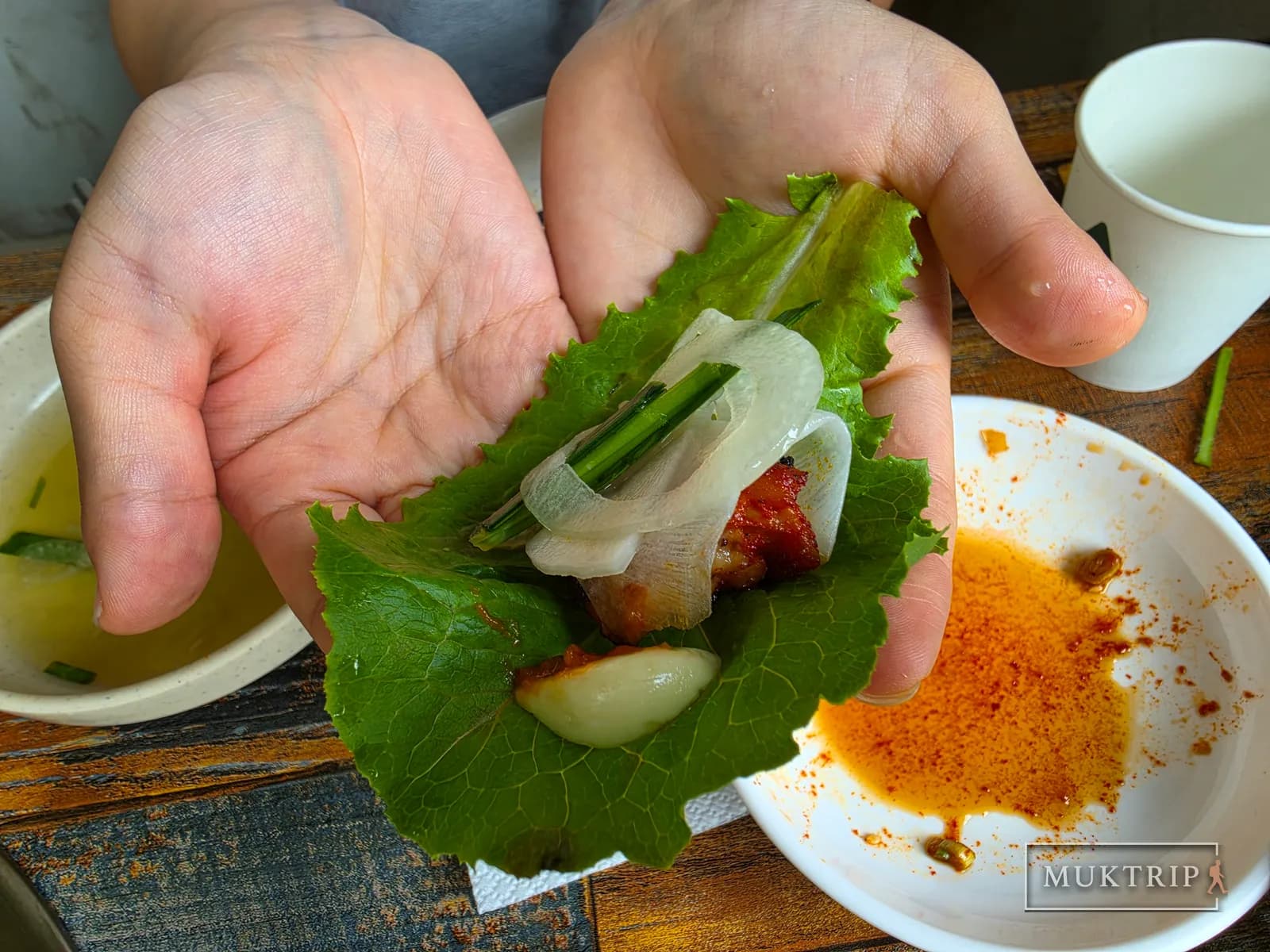 A hand holding a lettuce wrap topped with grilled meat, onion, chives, and garlic