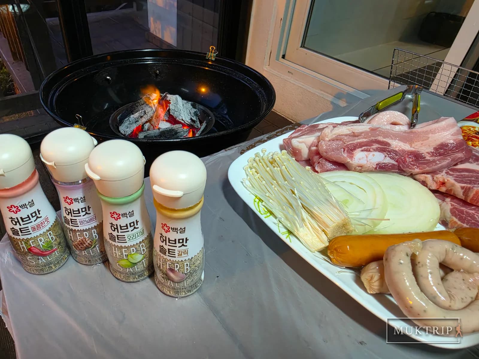 Four bottles of herb-flavored salt, a charcoal brazier, and a plate of meat
