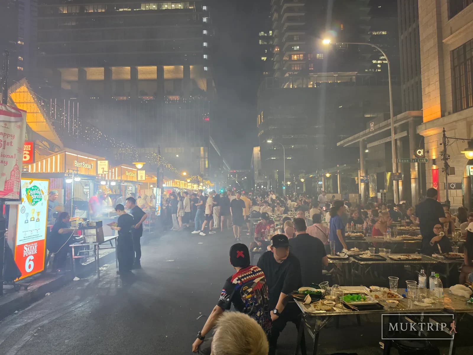 Crowds seated at outdoor tables amid smoke on Satay Street beside Lau Pa Sat