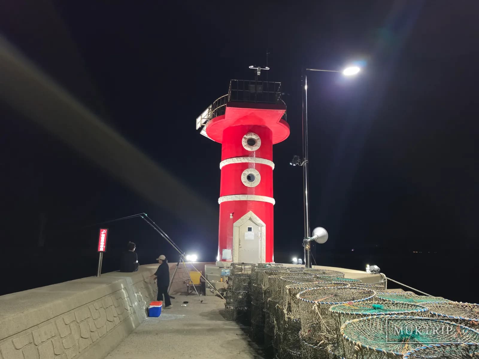 夜の海の防波堤に立つ赤い灯台と釣りをする人々