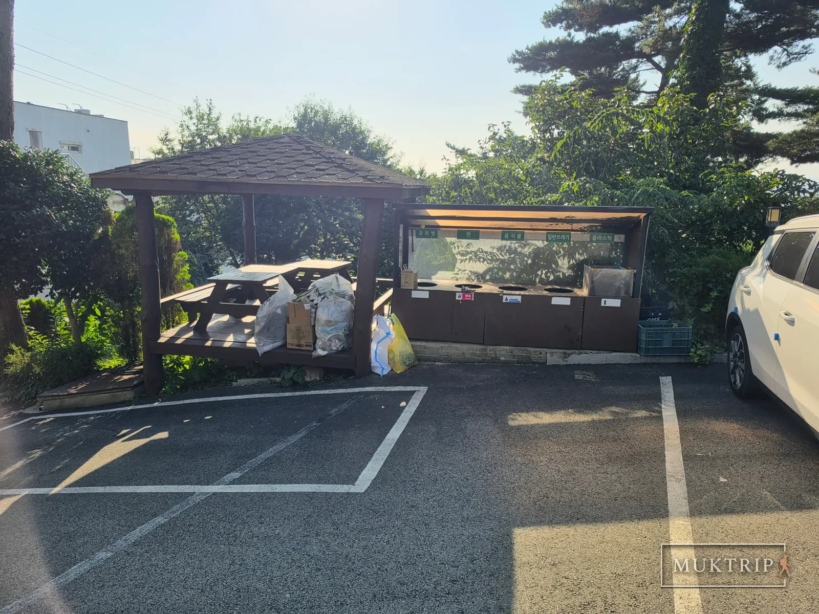 A gazebo and recycling bins beside the parking lot of a pension in Taean