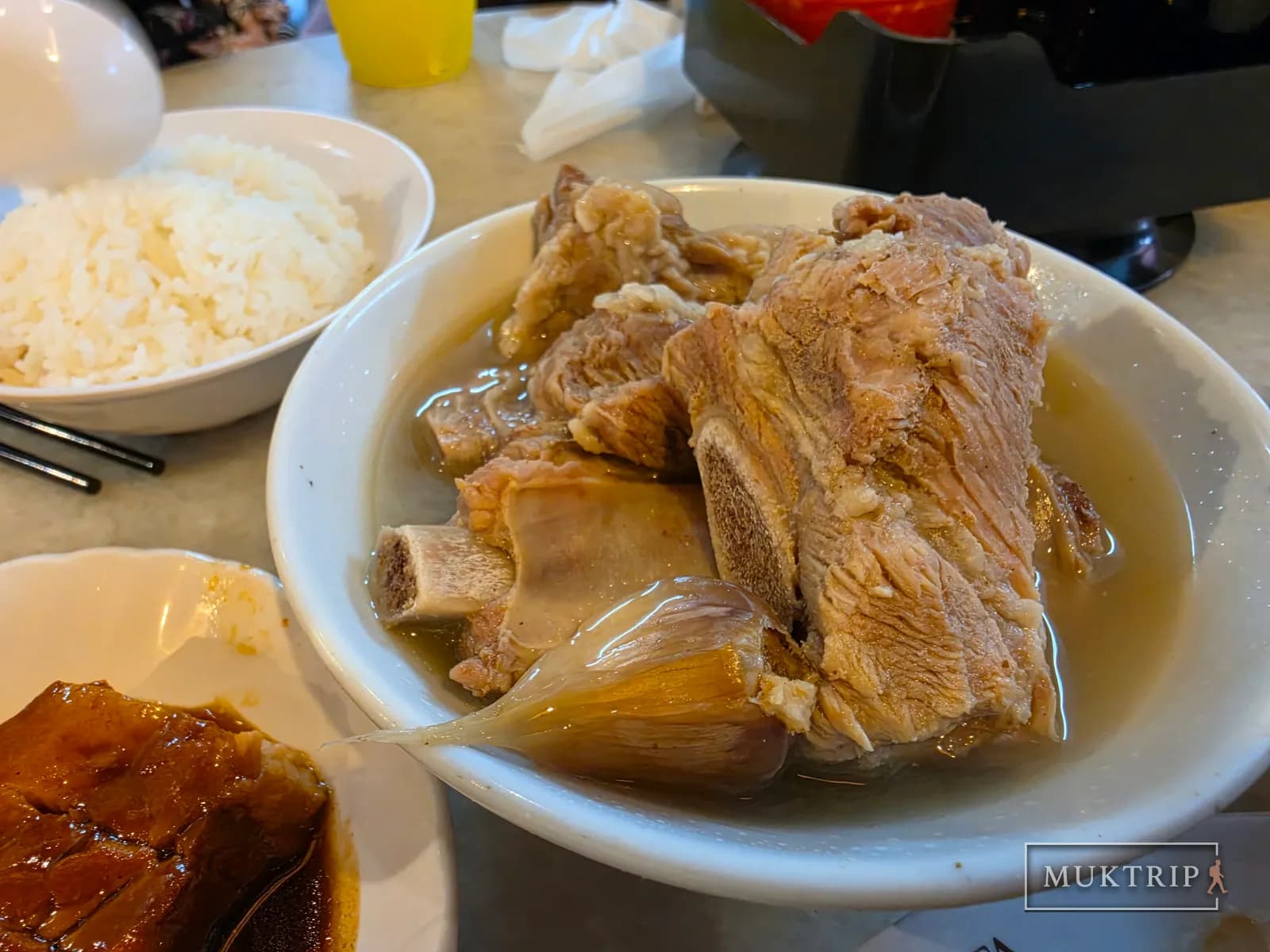 A bowl of clear bak kut teh broth with garlic and large pork ribs