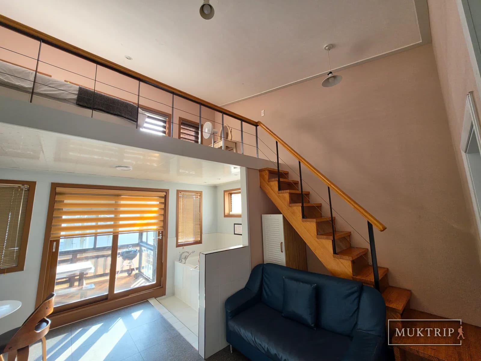 A room with a wooden staircase leading to the loft, a sofa, and a spa tub on the first floor
